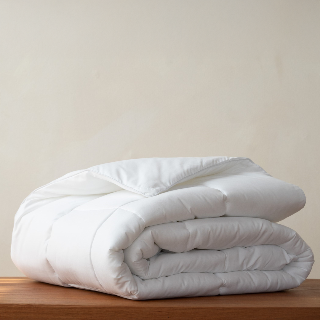 The Down Duvet, a white duck down duvet insert, folded on a wooden bench